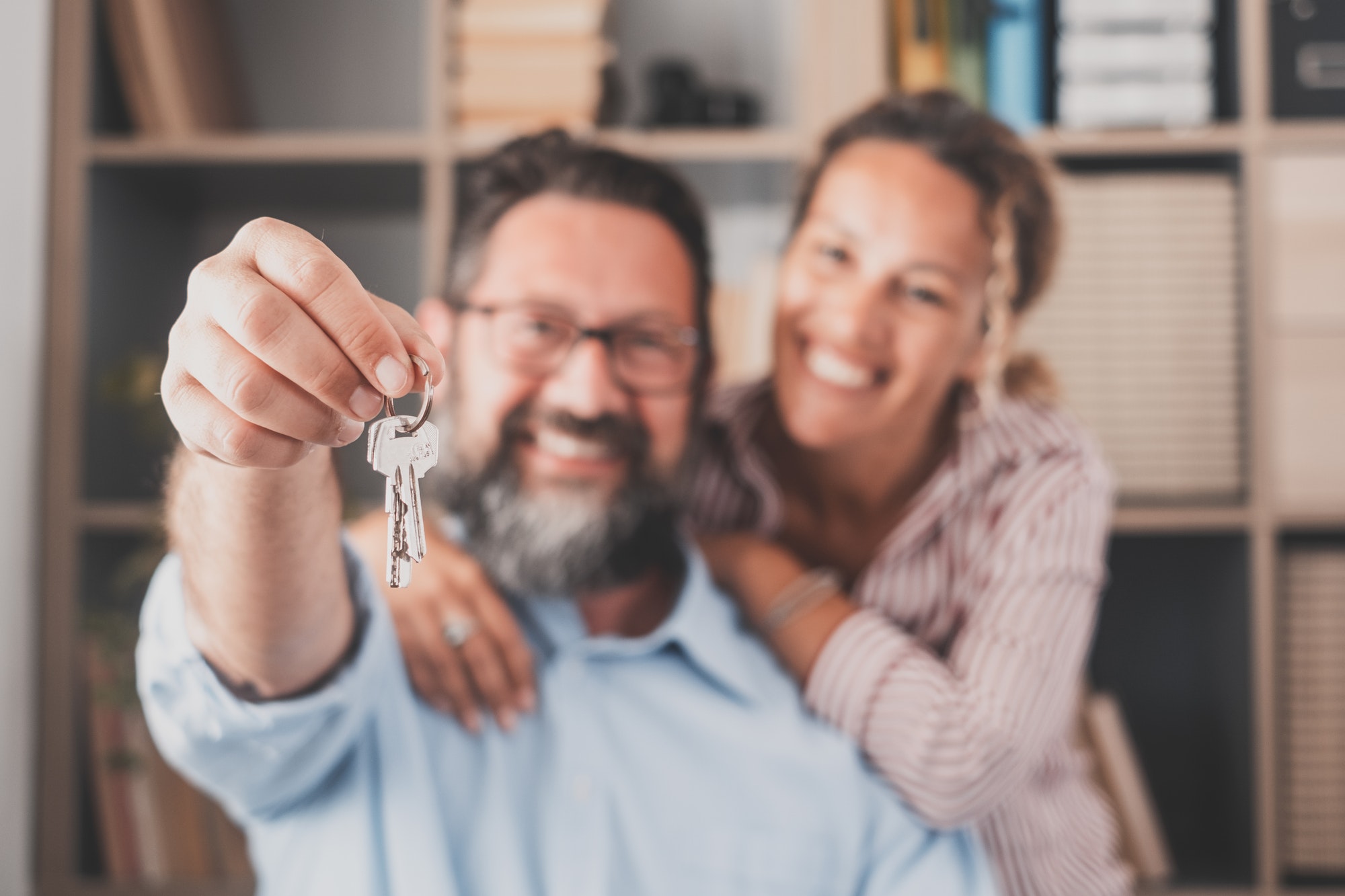 Focus on keys, held by excited young spouses homeowners. Happy married family couple