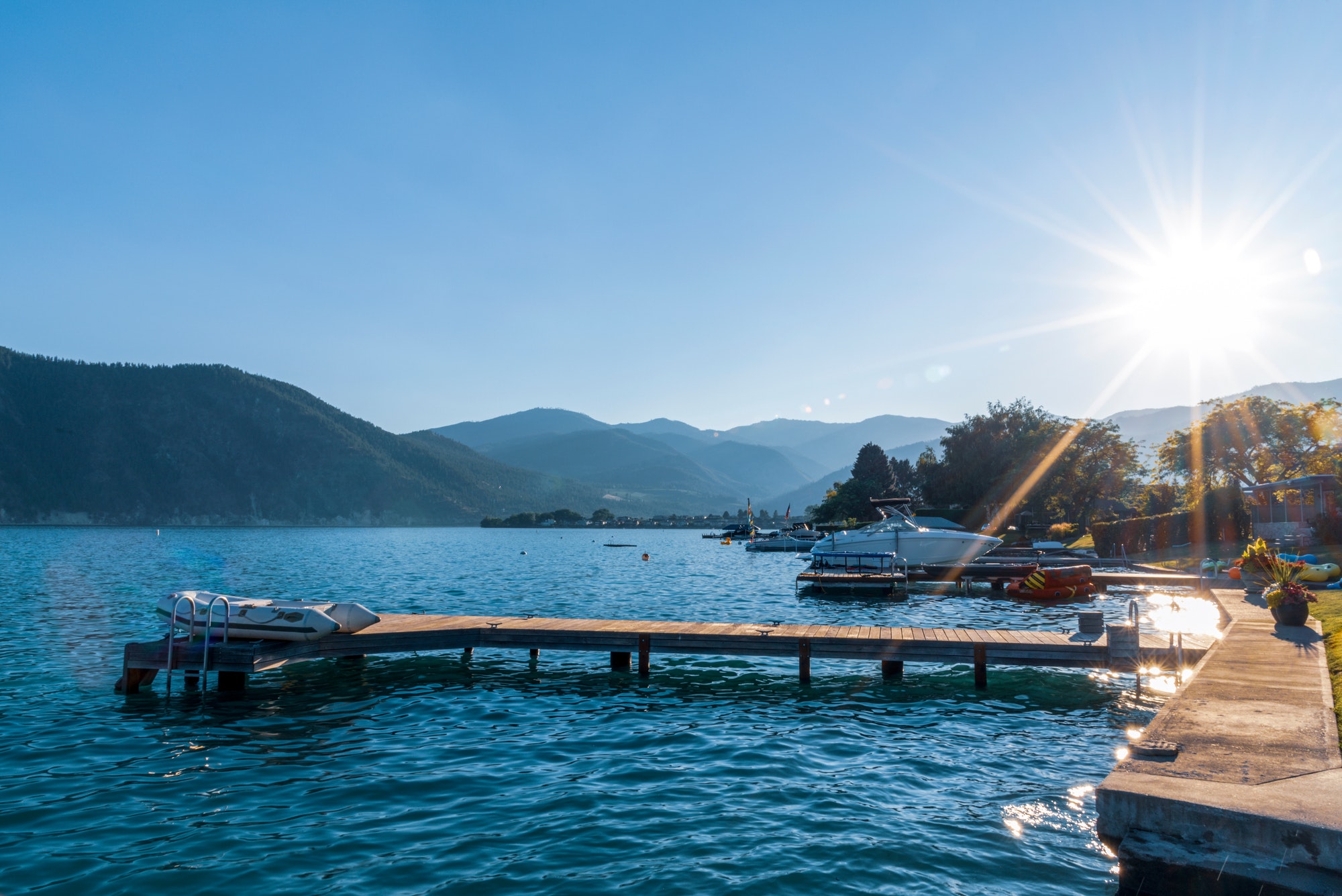 Lake shore boat dock with small inflatable dingy raft late day sunburst sunshine over mountains.